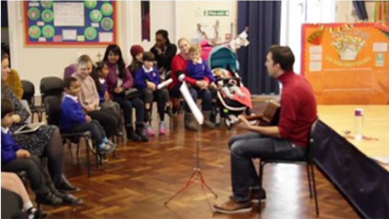 A man in a school auditorium playing guitar to a group of children