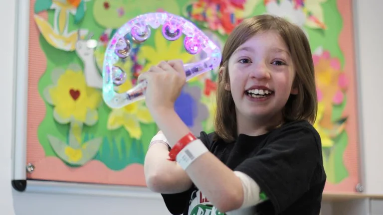 A child in a hospital setting smiles while shaking a tambourine. 