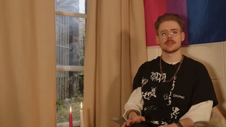 Producer talking to camera with LGBTQI+ flag behind