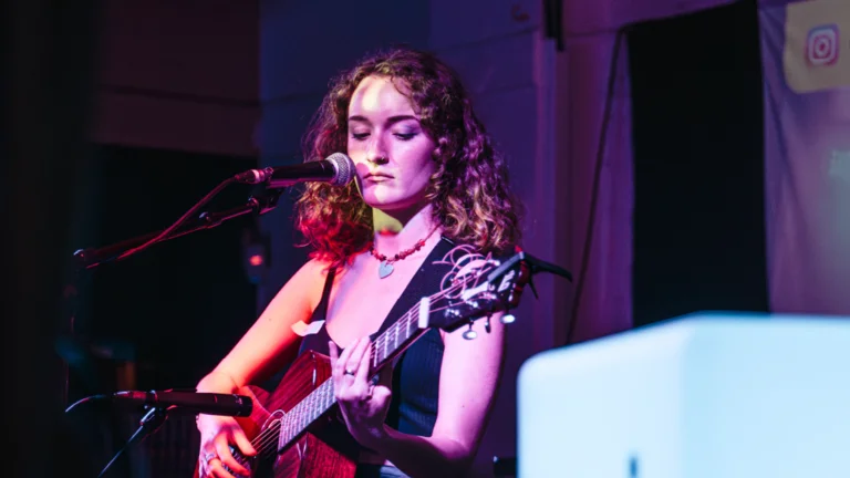 a woman with brown curly hair plays acoustic guitar on stage