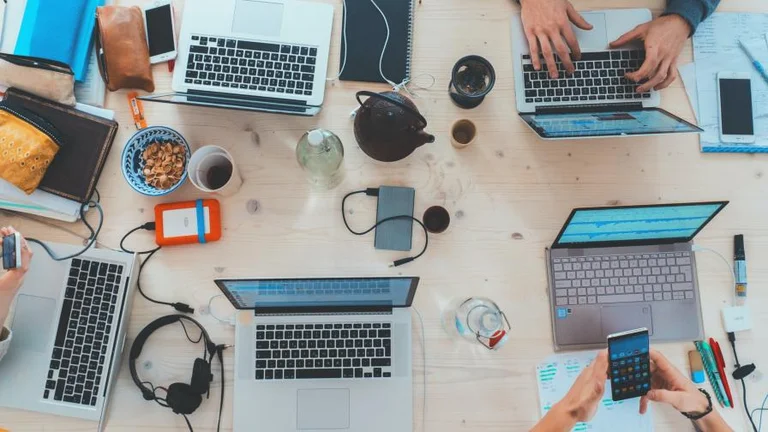 A top down view of a desk with multiple people working on laptops