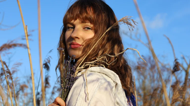 a woman with way brown hair and a fringe looks at the camera. She is in a wheat field.