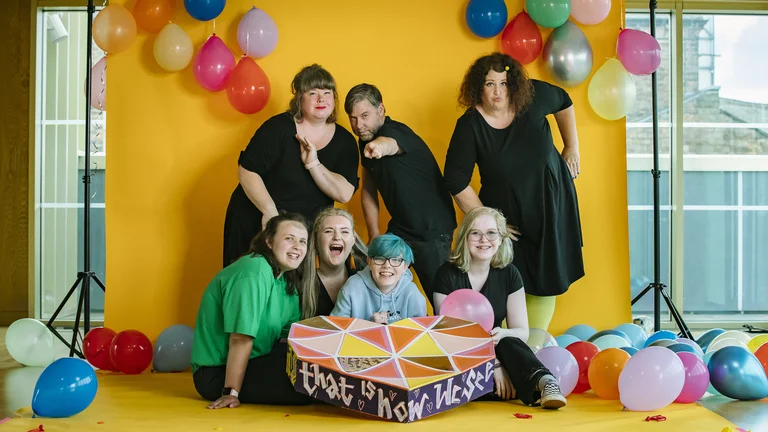 Picture of project The Next Big Thing with seven people smiling close to a yellow background with ballons