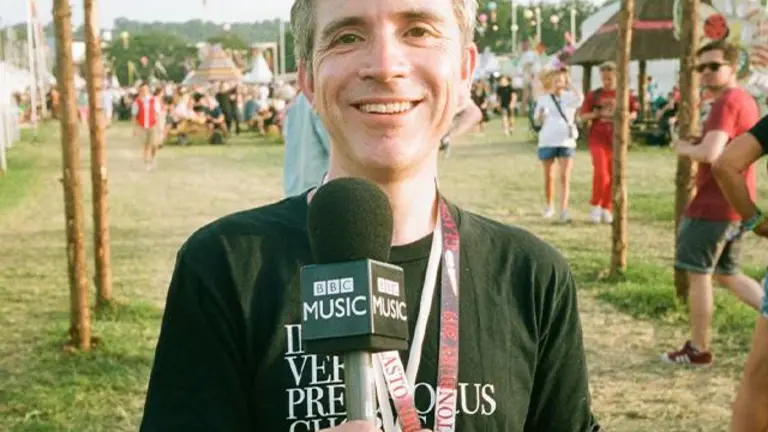 Mark Savage holds a microphone and reports from a festival