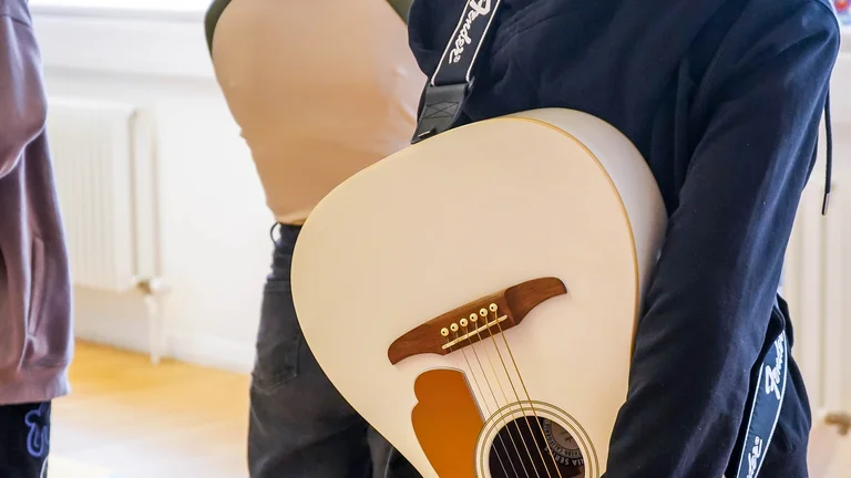 Image of three young people with their backs to the camera, a white acoustic guitar behind one of their backs