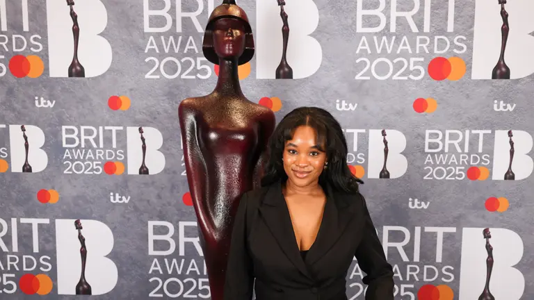 maya egbo poses in front of a branded Brit awards wall and brit awards statue
