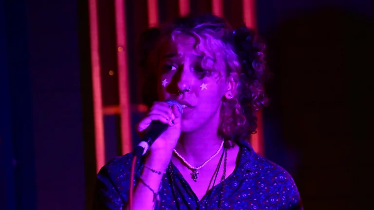 a person with curly hair in pigtails sings into a mic