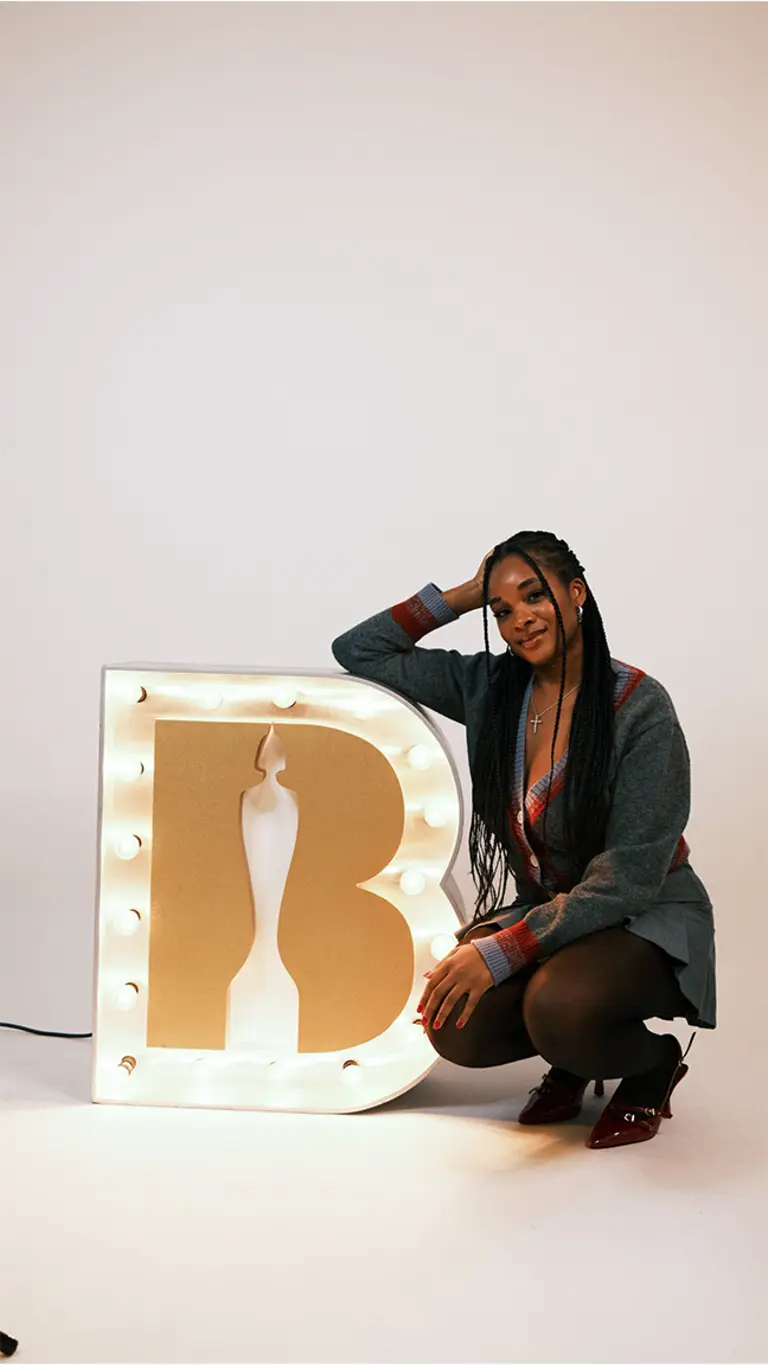 maya poses next to an illuminated brits logo sign