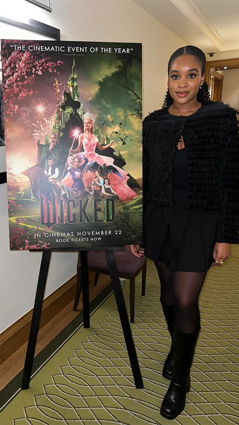 maya stands next to a wicked movie poster