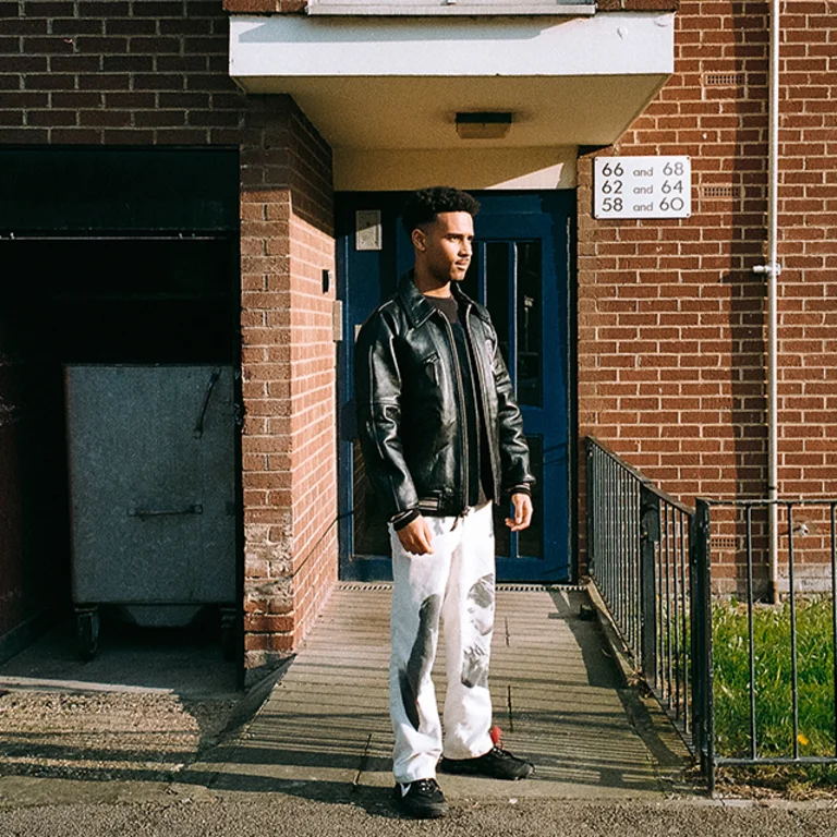 a person wears a black leather jacket and stands outside a building