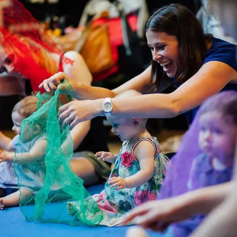 Woman smiling playing with green material with happy baby in a group project