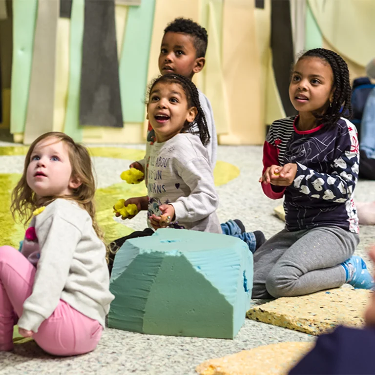 4 delighted children looking up, beyond the camera, smiling, holding colourful blocks