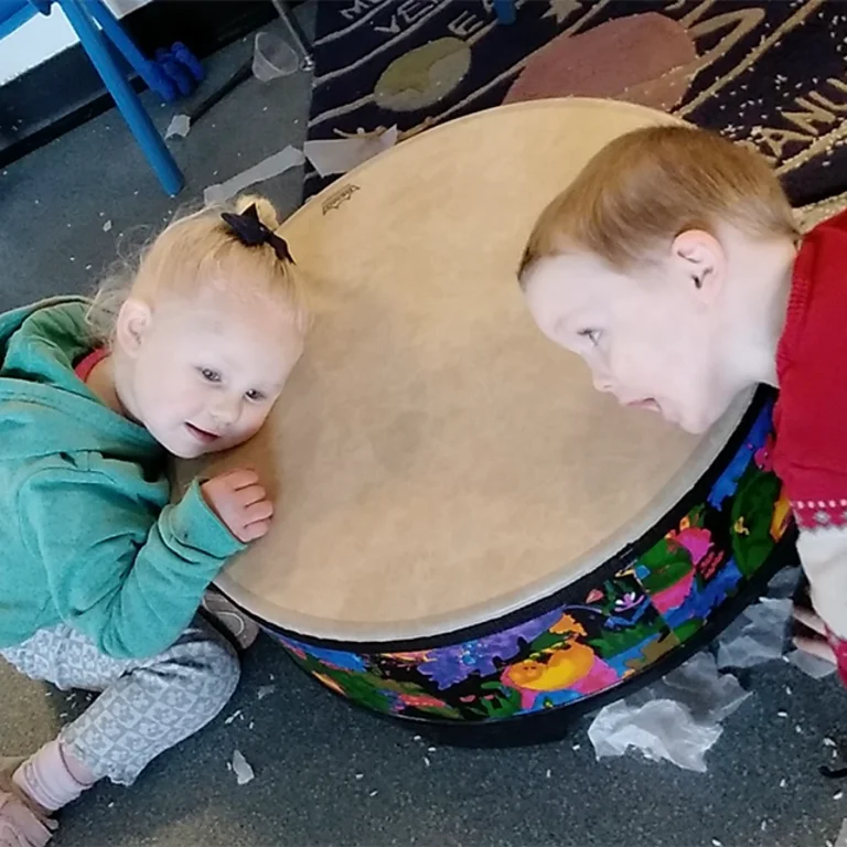 Two children laying their head against a large drum